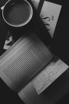 an open book sitting on top of a table next to a cup of coffee and envelopes