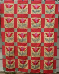 a red and yellow quilt hanging from a clothes line with flowers in the center on it