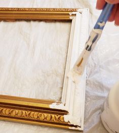 a person is painting a gold frame with white paint