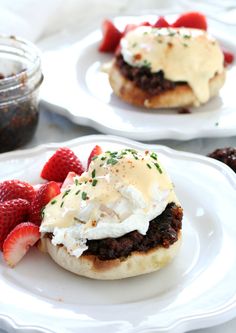 two white plates with food on them and some strawberries in the middle one plate has an open face sandwich