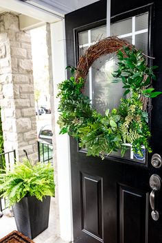 a wreath on the front door of a house with potted plants and a welcome mat