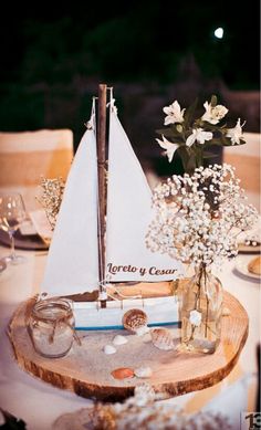 a small sailboat is sitting on a table with flowers and seashells in it