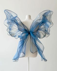 a white mannequin with blue sheer ribbon on it's back and wings