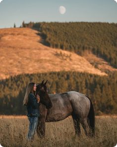 a woman standing next to a horse in a field