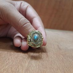 a hand holding a ring with a turquoise stone in it on top of a wooden table