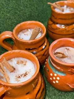 four orange mugs with cinnamon sticks in them on green carpeted floor next to each other