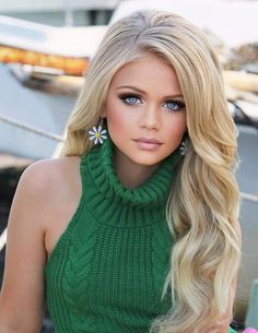 a barbie doll with long blonde hair wearing a green turtle neck sweater and flower earrings