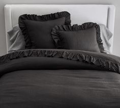 a bed with black ruffled sheets and pillows