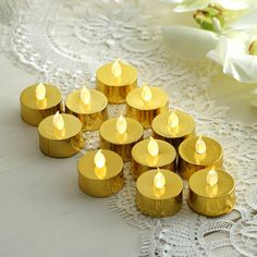 small gold tealight candles are lined up on a lace doily with flowers in the background