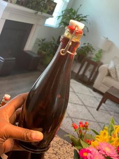 a person holding a bottle in front of a fireplace with flowers on the table behind it