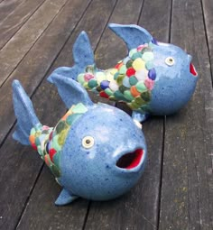 two ceramic fish sitting on top of a wooden deck