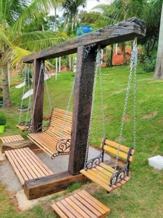 a wooden swing with chains hanging from it's sides in the grass near some palm trees