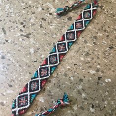 a braided bracelet with tassels is laying on the ground next to a pair of scissors