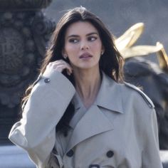 a woman in a trench coat is talking on her cell phone