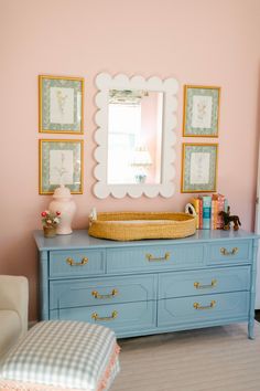 a baby's room with pink walls, blue dressers and pictures on the wall