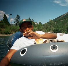 a man is sitting in an inflatable boat on the water with mountains in the background