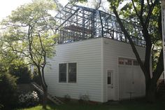 a small white house with a metal roof and balcony on the top floor is surrounded by trees