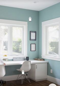 two white chairs sitting at a desk in front of three windows with blue paint on the walls