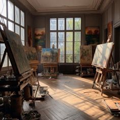 an artist's studio with lots of easels and paintings on the walls, in front of large windows