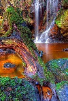 a waterfall with moss growing on the rocks and water running down it's sides