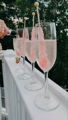 three champagne flutes are lined up on a balcony railing with pink confetti in them