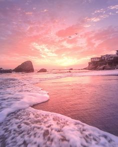 an ocean beach with waves coming in to shore and a pink sky above the water