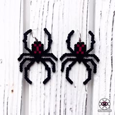 two black and red spider earrings are hanging on a white wooden wall with wood planks