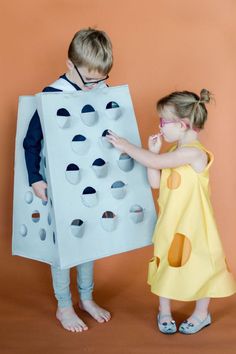 two children dressed in costumes standing next to each other, one holding a giant piece of cardboard