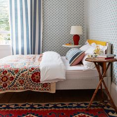 a bedroom with blue and white wallpaper, striped curtains and a bed in the corner