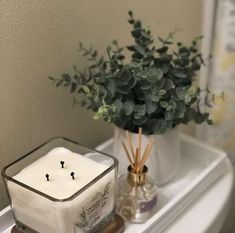 a white candle sitting on top of a bathroom counter next to a vase with flowers