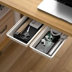 an open drawer with scissors and other items in it next to a laptop on a desk