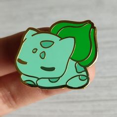 a hand holding a green and black pin with a cat on it's back