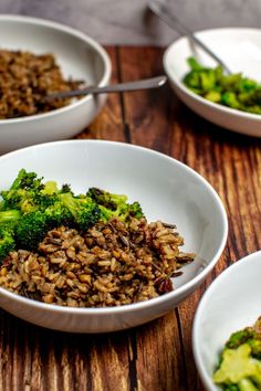 three bowls filled with rice and broccoli on top of a wooden table next to silverware