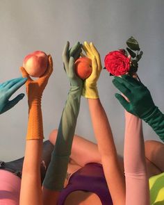 four women in colorful dresses and green gloves are holding up their hands with flowers on them