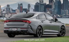 the rear end of a silver car driving down a road near a city skyline with tall buildings