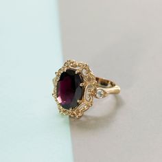 Elegant statement vintage style ring in 14k yellow gold, garnet and white cubic zirconia halo engagement, wedding or promise ring for women.   This impressive handmade ring is made of solid 14k yellow gold and is set with a big faceted oval red garnet, in a vintage style setting. Two smaller round white cz gems are set in a marquise setting, one on each side. The deep color of the gemstones combined with the unique design give this ring a bling chic that cannot be ignored.   Garnet is January's Gold And Garnet Ring, Antique Ruby Ring Gold, Ruby Engagement Ring Gold Vintage, Big Gemstone Rings, Ruby Red Engagement Ring, Garnet Engagement Ring Vintage, Colored Engagement Rings Vintage, Antique Engagement Rings Vintage 1920s, Big Engagement Ring