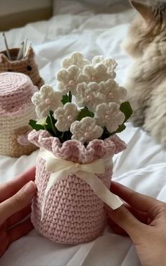 a person holding a small crocheted vase with flowers in it next to a cat