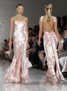 two women in pink dresses walking down the runway