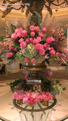 a large vase with pink flowers and greenery on top of a table in front of a chandelier