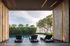 two lounge chairs sitting on top of a pool next to tall wooden pillars with trees in the background