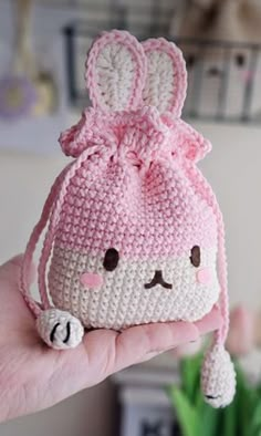 a hand holding a small crocheted bag with a pink bow on it's head