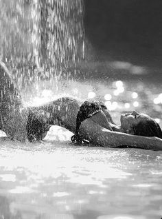 two people are laying down in the water and splashing them with their heads together