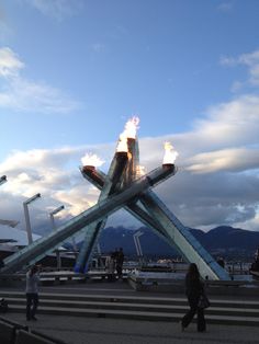 people are walking around in front of an art sculpture with flames coming out of it