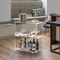 a bar cart with wine glasses and liquor bottles on it in front of a couch