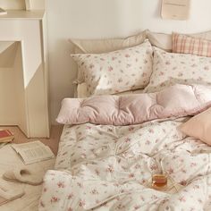 an unmade bed with pink and white flowers on it, next to a book shelf