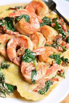 pasta with shrimp, spinach and cheese on it in a white plate next to a fork