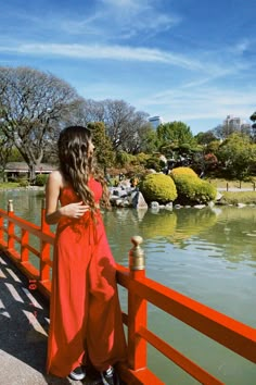 a woman in an orange dress is standing on a bridge over water and looking at the sky