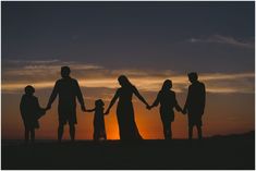 a group of people holding hands while standing on top of a sandy beach at sunset