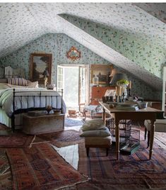 an attic bedroom with a bed, desk and chair in the corner is decorated with floral wallpaper