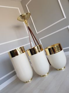 three white vases with gold trim hanging from a ceiling fixture in a living room